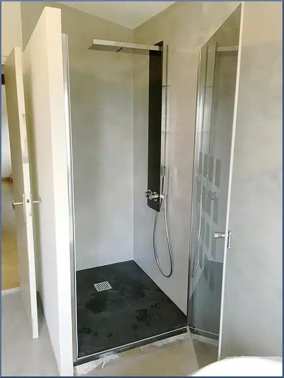 Douche à l'italienne moderne avec parois gris béton, receveur foncé, pommeau pluie et paroi vitrée décorée.