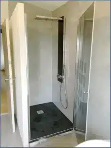Douche à l'italienne contemporaine aux murs gris texturés, receveur noir, colonne de douche pluie et porte vitrée à motifs.
