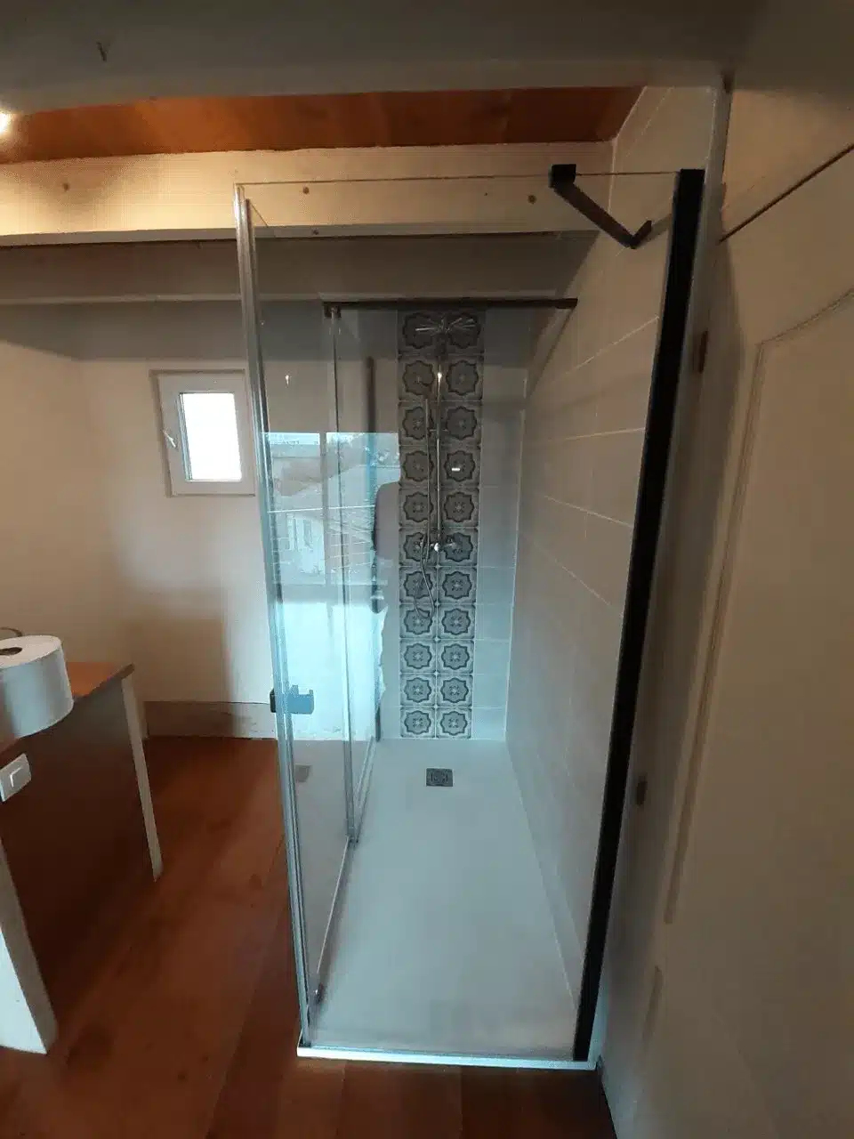 Douche italienne moderne avec paroi en verre, carrelage décoratif bleu/gris et sol clair. Plancher bois, plafond poutres.