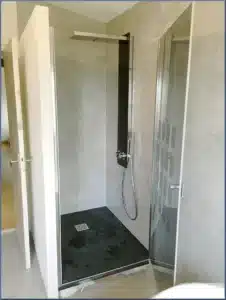 Douche moderne avec receveur noir, murs gris texturés et pommeau de pluie design. Paroi vitrée élégante. Salle de bain contemporaine.