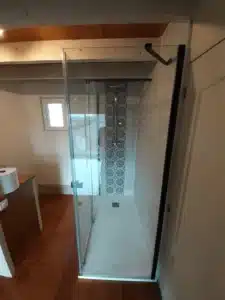 Douche à l'italienne moderne avec parois en verre, carrelage gris clair et bande décorative à motifs. Sol en bois clair.