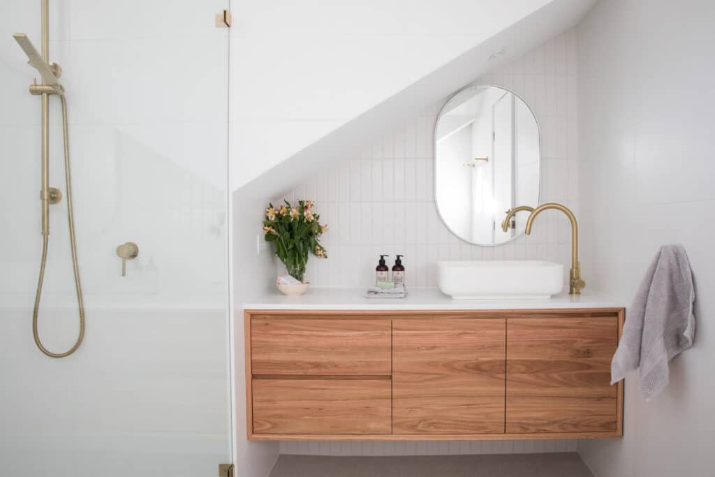 Salle de bain moderne | Design élégant blanc & bois Salle de bain moderne blanche: douche et robinet dorés, meuble-lavabo en bois clair, vasque blanche, miroir ovale.