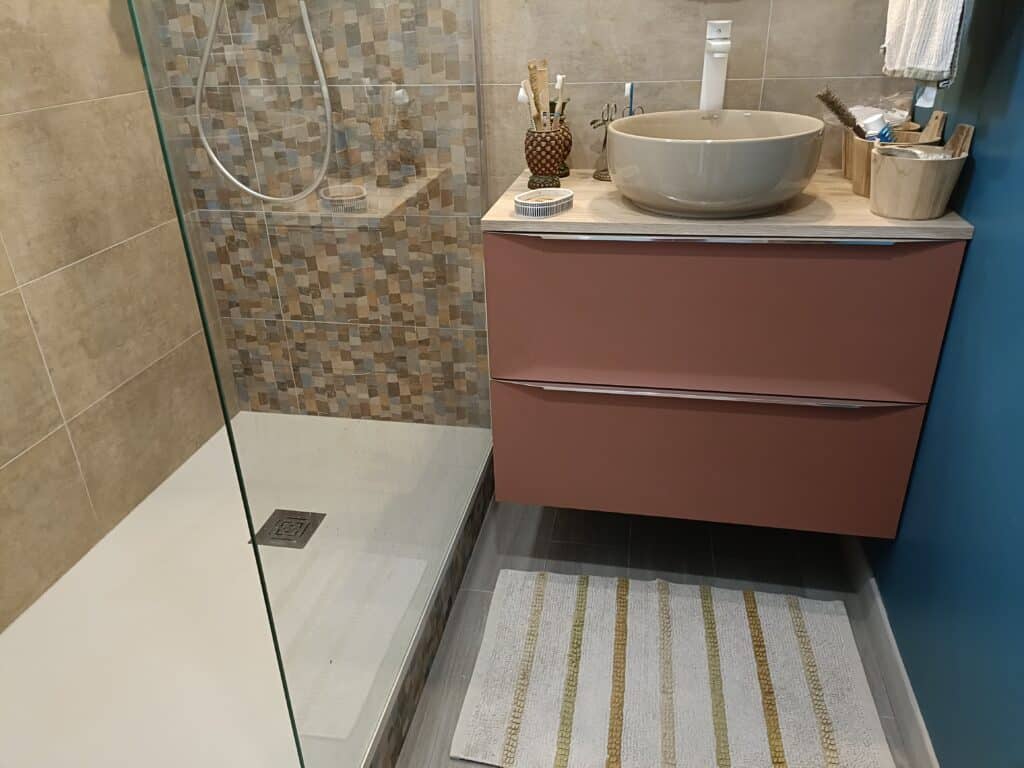 Salle de bain moderne avec douche à l'italienne, meuble-lavabo suspendu terracotta, vasque ronde beige et robinet haut blanc. Mur mosaïque.