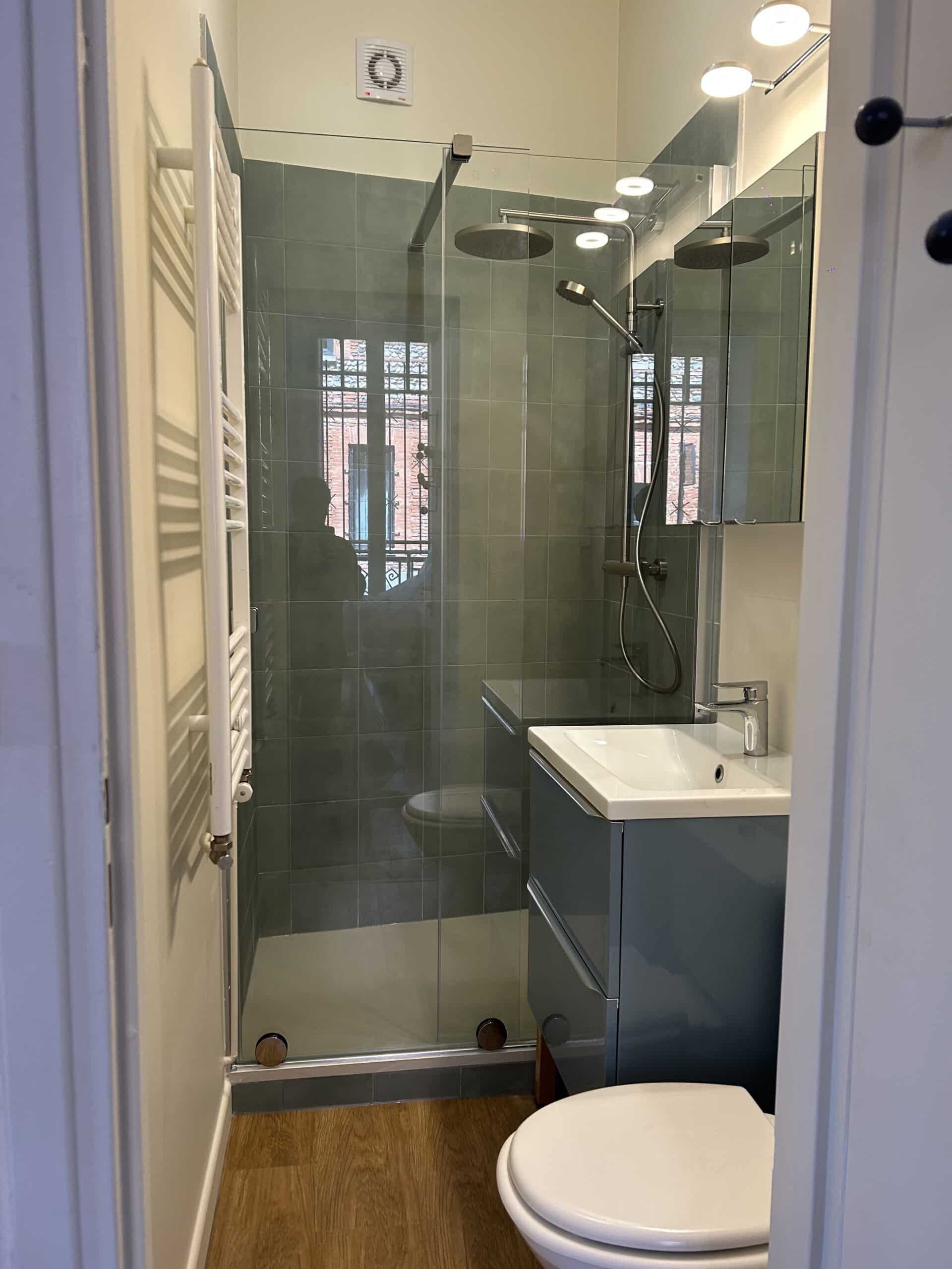 Salle de bain moderne : douche à l'italienne, carrelage vert, meuble vasque bleu et toilettes blanches.