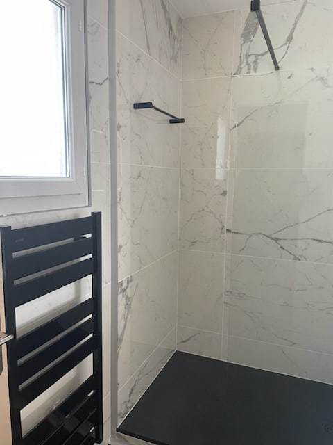 Douche moderne avec carrelage effet marbre blanc, receveur noir et sèche-serviettes noir design.