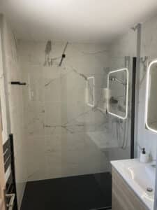 Douche à l'italienne avec marbre blanc, sol noir et miroir rétroéclairé.