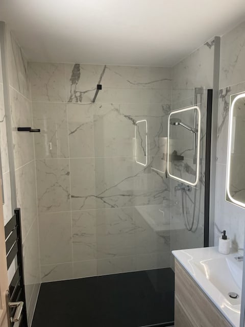 Douche à l'italienne avec marbre blanc, sol noir et miroir rétroéclairé.