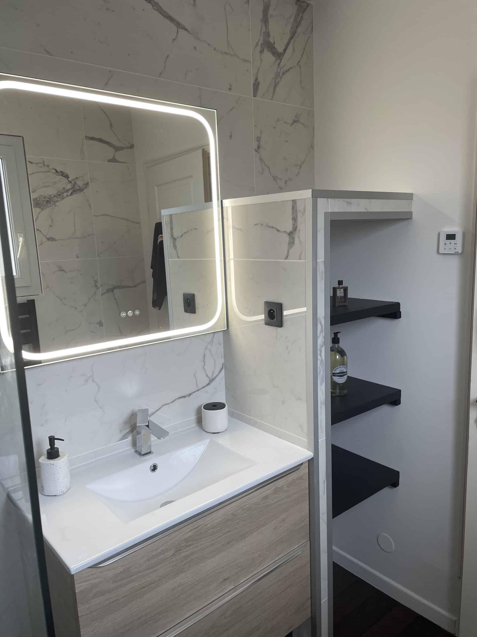 Salle de bain moderne avec miroir LED rétroéclairé, carrelage effet marbre et meuble vasque en bois clair.