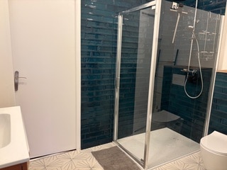 Salle de bain moderne avec douche à paroi vitrée, carrelage bleu canard et sol géométrique étoilé.