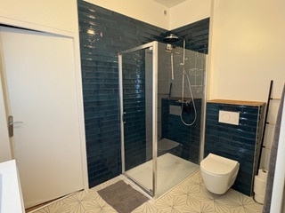 Salle de bain moderne avec douche à l'italienne, carrelage bleu et sol à motifs géométriques.