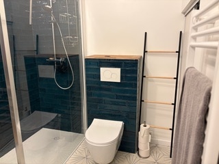 Salle de bain moderne avec douche à l'italienne, WC suspendu sur carrelage bleu canard et échelle décorative.