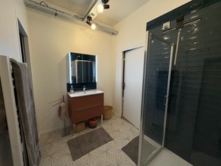 Salle de bain moderne avec meuble vasque marron, miroir rétroéclairé, douche vitrée et sol à motifs géométriques.
